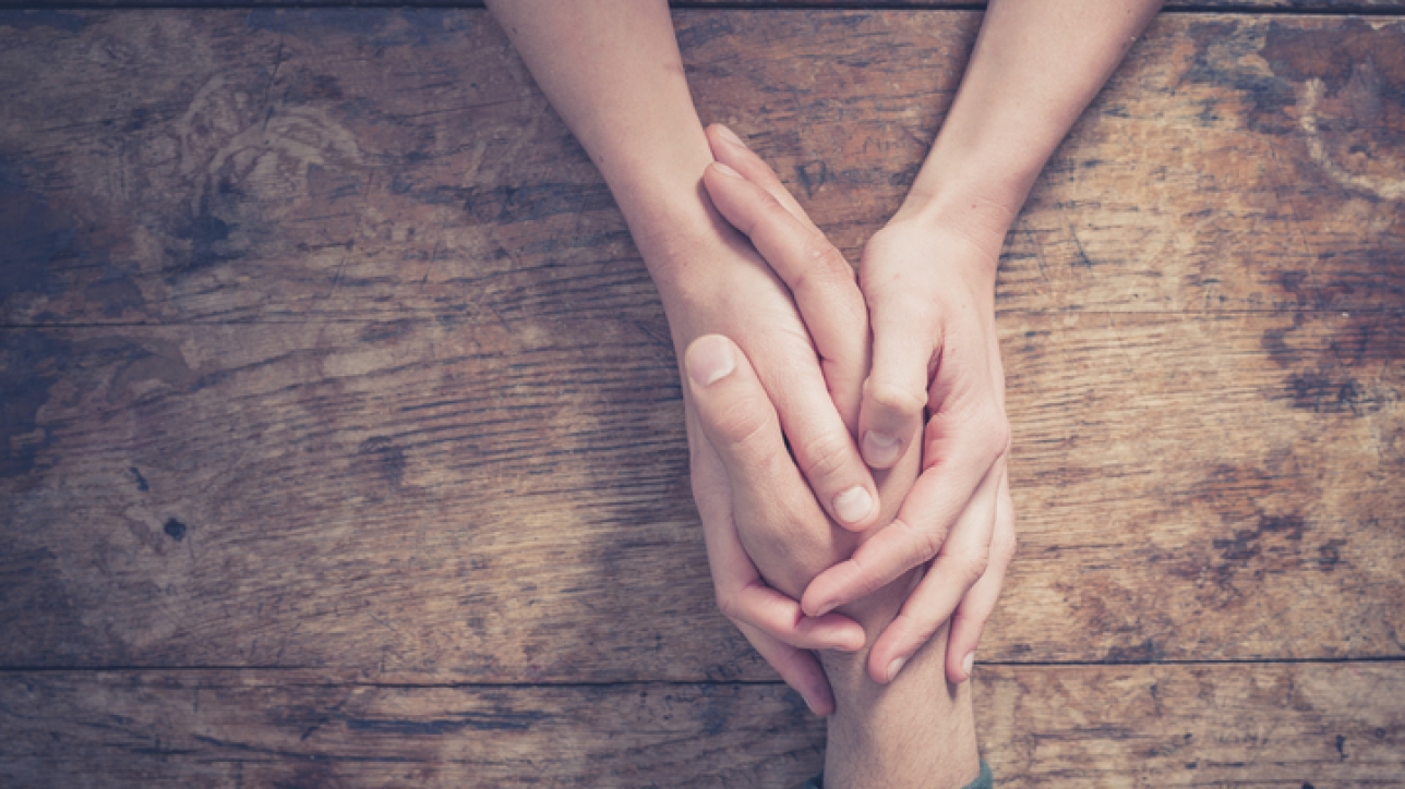 Close up on a man and a woman holding hands at a wooden table